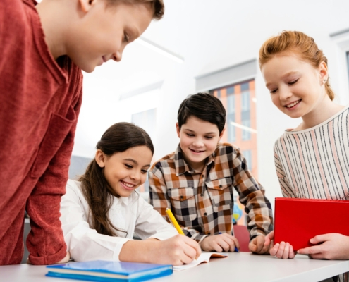 Smiling pupils with notebook and books discussing in classroom