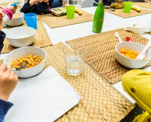 Children sitting at the table in a school cafeteria while the teachers serve them food.