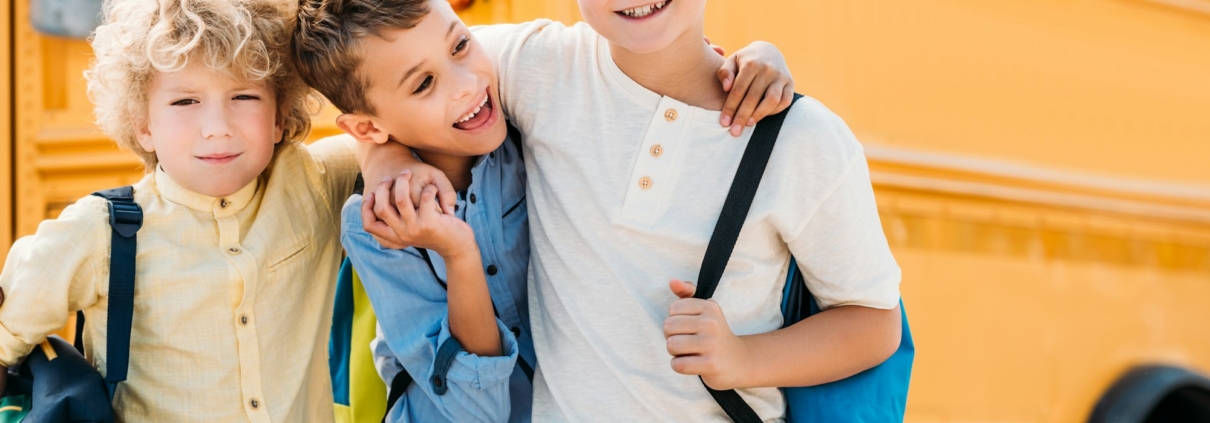 happy little schoolboys embracing in front of school bus