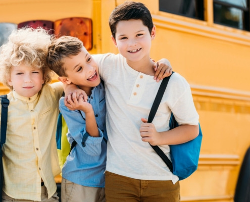 happy little schoolboys embracing in front of school bus