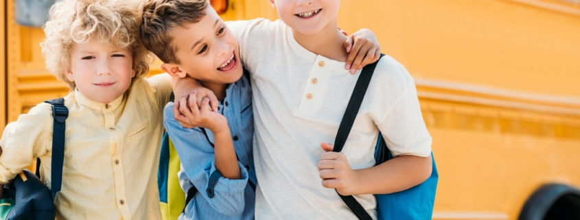 happy little schoolboys embracing in front of school bus